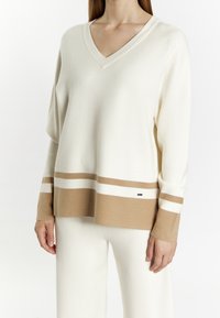 Cream-colored pullover with a V-neck, featuring light brown and white horizontal stripes at the hem and cuffs, made of soft material.