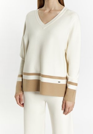 Pull crème à col en V, avec des rayures horizontales marron clair et blanches au bas et aux poignets, fabriqué dans un matériau doux.