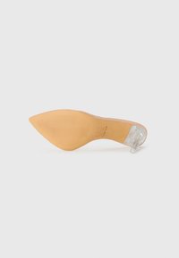 Chaussure à talon aigu en beige avec un talon stiletto en plastique transparent, vue de la semelle sur fond blanc.