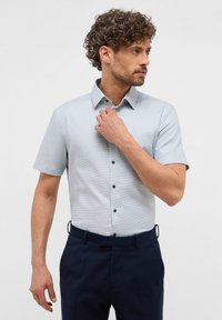 Camicia azzurro chiaro a maniche corte con motivo a quadretti, colletto button-down e bottoni scuri, abbinata a pantaloni blu navy.