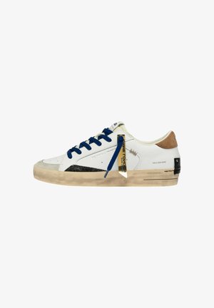 Sneaker bianca bassa con lacci blu, suola beige, accenti neri e color cuoio, e una targhetta dorata appesa ai lacci di lato.