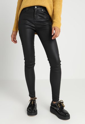 Zwarte neplederen skinny broek met een hoge taille, gecombineerd met zwarte plateau schoenen en een gestructureerde mosterdkleurige trui.