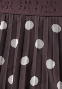 Tissu plissé sombre avec de grands pois blancs et une taille texturée présentant des lettres brodées.
