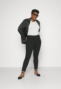 Chaqueta de satén negra, top ajustado blanco, jeans negros ajustados y bailarinas negras con tiras en el tobillo. La modelo lleva gafas de sol negras de gran tamaño.
