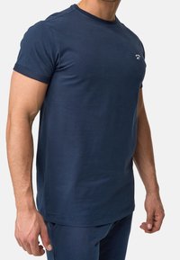 Marineblaue Kurzarm-T-Shirt aus weicher Baumwolle, mit Rundhalskragen und einem kleinen weißen Logo auf der Brust. Glatte Textur.