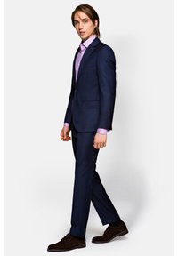 Granatowy garnitur w kratkę, dopasowany krój, uzupełniony jasnofioletową koszulą. Brązowe zamszowe buty dopełniają całość.