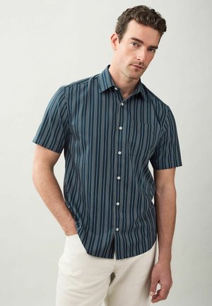 Camisa de manga corta en verde azulado oscuro con rayas verticales blancas, que presenta un cuello abotonado y un solo bolsillo en el pecho. Tejido de mezcla de algodón.