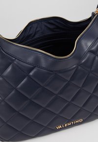 Quiltad marinblå läderväska med guldtonad dragkedjestängning och subtil branding, med en slät yta och ett rymligt inre.