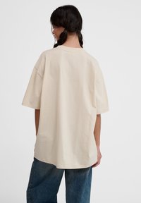 Beige oversized t-shirt lavet af bomuld, med korte ærmer, rund halsudskæring og lige kant, parret med blå denim jeans.
