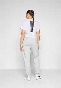 Bela skrčena majica s črnimi navpičnimi črtami na hrbtni strani, v kombinaciji s svetlo sivimi trenirkami in belimi športnimi čevlji.