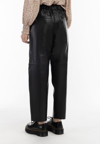Zwarte leren broeken met een elastische tailleband, rechte pijpen en achterzakken; in combinatie met zwarte schoenen met een dikke zool.