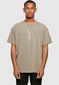 Korte ærmer, oversized t-shirt i dæmpet taupe med en hvid kursiv "Faith" grafik på forsiden; bomuldsstof med en blød tekstur.