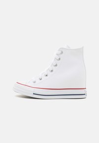 White high-top canvas sneakers with a rubber sole, red stripe accent, round toe, and eyelets for laces, featuring a textured surface.