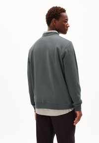 Sweatshirt gris foncé avec un col arrondi, des poignets et un ourlet côtelés, superposé sur une chemise à carreaux claire, vu de l'arrière.