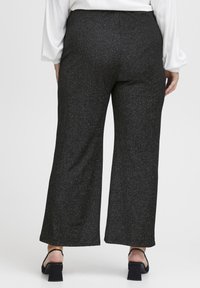 Svarta vida byxor med en texturerad, glittrande yta. Har en elastisk midja och en luftig siluett. Kombineras med svarta blockklackade sandaler.