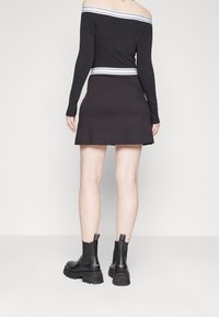 Musta pitkähihaisen olkapäät paljastavan yläosa, jossa valkoinen raidetaiiluwi, yhdistetty mustaan levenevään minihameeseen. Mustat nilkkurit paksuilla pohjilla.