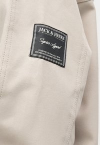 Bežna tkanina z finim teksturo; vsebuje črno oznako z belim besedilom, ki navaja "JACK & JONES" in "Superior Apparel." Vidna elegantna vezava.