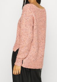 Roze gebreide trui met een losse pasvorm, geribde halslijn en zijopeningen. Het gestructureerde garen bevat spikkels van paars en oranje. Lange mouwen.