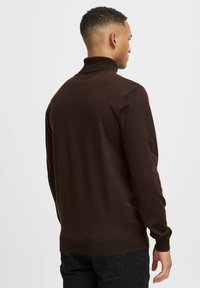 Maglione a collo alto marrone con un finish testurizzato, collo e polsini a coste, peso medio, silhouette aderente e design posteriore pulito e senza cuciture.