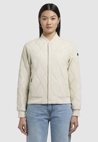 Quiltad beige bomberjacka med ståkrage, åtsittande ärmslut och sidofickor. Har en texturerad yta och en dekorativ emblem på ärmen.