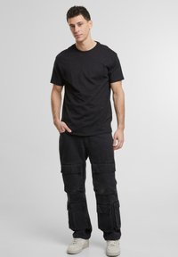 Un tricou negru din bumbac cu guler rotund, purtat cu pantaloni cargo negri care au multiple buzunare și o croială puțin mai lejeră. Adidași albi.
