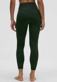 Højtsiddende, tætsiddende leggings i mørkegrøn lavet af strækbart materiale med en glat tekstur og diskrete sømdetaljer.