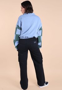 Pull en fleece bleu clair avec des manches rayées vertes et blanches, taille élastique ; associé à un pantalon cargo noir et des baskets noires.