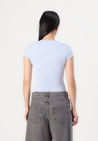 T-shirt ajustado azul claro com mangas curtas, textura suave e decote redondo, combinado com jeans cinzentos folgados com dois bolsos traseiros.