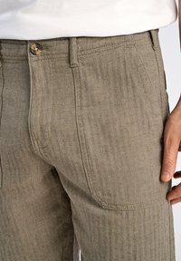 Beige broek met visgraatpatroon en een rechte snit. Voorzien van een enkele knoopsluiting, voor- en achterzakken, en een gemêleerd stof.