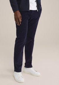 Marina blå kordflorsbyxor med tapered fit, med en texturerad yta och sidofickor, tillsammans med vita låga sneakers.