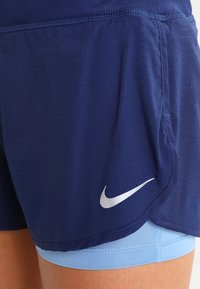 Laivaston siniset urheilushortsit, joissa on reikäkudos, vaaleansininen sisäkerros ja sivulla heijastava hopeanvärinen Nike-logo.