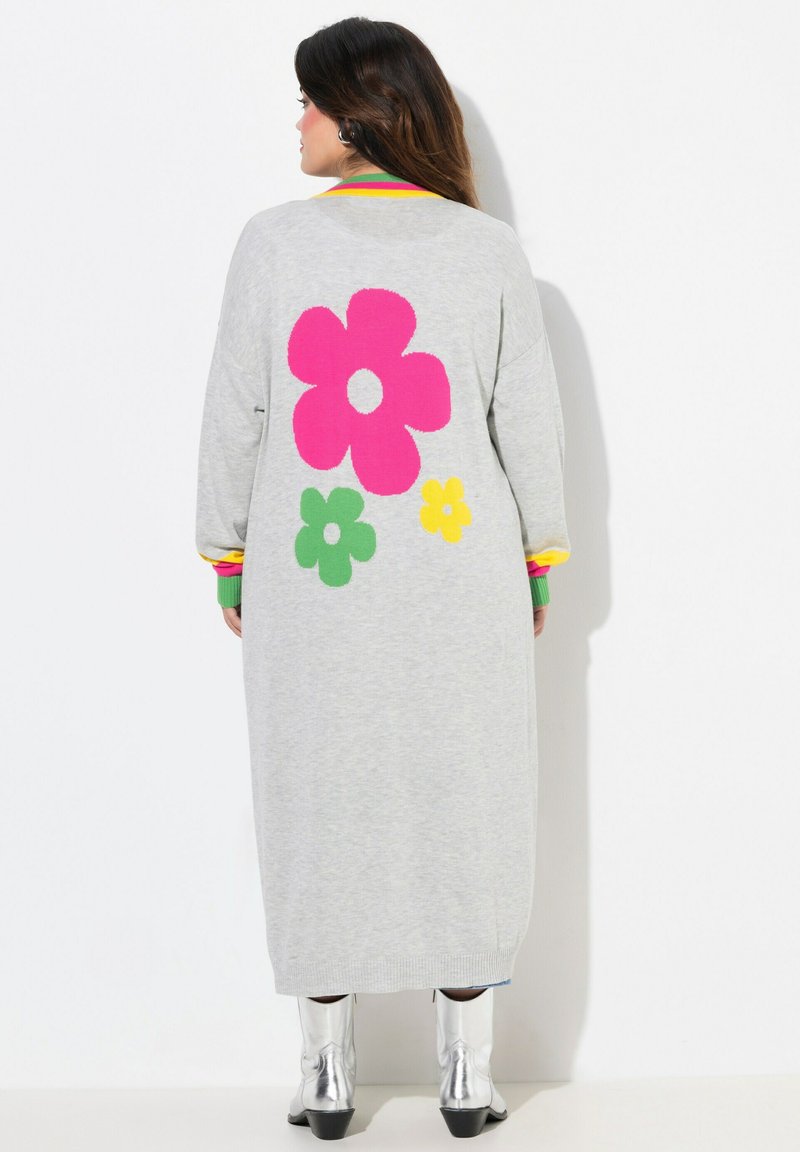 Lange, grijze gebreide cardigan met grote roze, groene en gele bloemmotieven op de achterkant. Beschikt over kleurrijke gestreepte manchetten en kraag.
