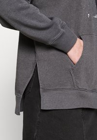 Sweat-shirt gris au design décontracté, avec poignets côtelés, fentes latérales et poche avant. Tissu doux avec une finition texturée.