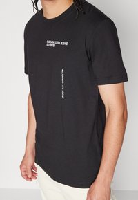 Svart bomulls t-shirt med rund hals, korta ärmar och tryckt text på framsidan och sidan i vitt. Standard passform med mjuk textur.