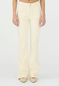 Pantalon évasé en ivoire, en matière douce, avec poches avant et un unique bouton en métal. Texture lisse, taille ajustée, design long.