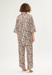 Bruin en beige gestreepte satijnen tweedelige set met een losvallend, kraagloos shirt en wijde broek. Glad textuur en ontspannen silhouet.