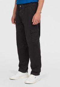 Black cargo pants with a loose fit, featuring side pockets, a classic button front, and cotton fabric. Worn with white sneakers.