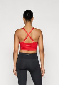 Red sports bra with adjustable cross-back straps, featuring a soft texture and logo detail. Paired with high-waisted black leggings.