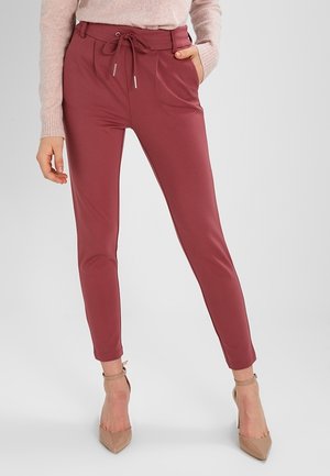 Mujer con pantalones ajustados de color rosa oscuro con cintura de cordón, combinados con un suéter rosa claro y zapatos de tacón beige.