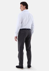Camicia a maniche lunghe a righe bianche, pantaloni grigi, cintura nera, scarpe scure. Tessuto liscio, vestibilità su misura. Cuciture posteriori visibili e dettagli con bottoni.
