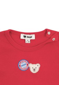 Red cotton t-shirt featuring a round neckline, snap buttons, and embroidered patches: a bear face and a Bayern München logo. Size tag: 62.