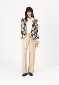 Zwarte blazer met hartpatroon, witte shirt, beigekleurige broek met zijstreep en zwarte schoenen. Soepele texturen en een getailleerd ontwerp.