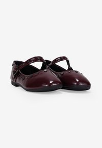 Bailarinas de charol burdeos con correas cruzadas, detalles de tachuelas a lo largo del borde superior y una puntera redondeada, con una suela de goma negra baja.