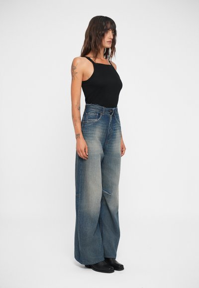 High-waisted, wide-leg denim jeans in light blue with faded areas; paired with a black fitted tank top and black ankle boots.