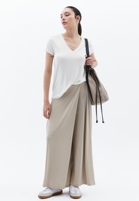 Camiseta blanca de cuello en V, pantalones anchos beiges y zapatillas blancas. Los pantalones tienen una tela drapeada y un ajuste relajado. Bolsa negra con cuerdas.