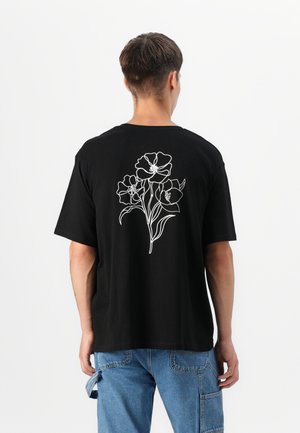 Zwarte katoen t-shirt met een witte florale omtrekontwerp op de achterkant, met een relaxte pasvorm en korte mouwen.