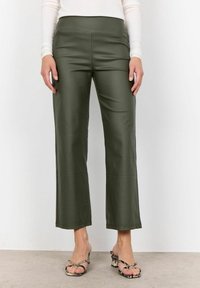 Oliwkowo zielone, wysokowcięte spodnie z ekologicznej skóry o prostym kroju i bezszwowym wykończeniu, zestawione z sandałami na obcasie z paseczkami.