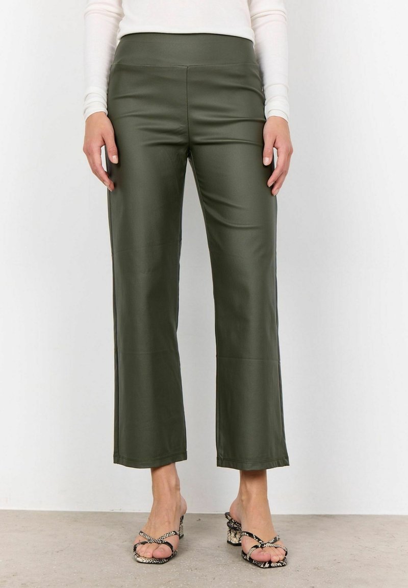 Oliwkowo zielone, wysokowcięte spodnie z ekologicznej skóry o prostym kroju i bezszwowym wykończeniu, zestawione z sandałami na obcasie z paseczkami.