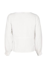 Vit långärmad blus med lös passform, texturerad tyg och en enkel rundad halsringning. Har elastiska ärmslut och en avslappnad bakseam.