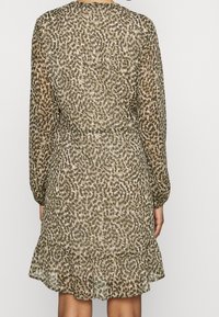 Brun mönstrad klänning med långa ärmar, samlad midja och volangkant. Tillverkad av ett lätt, genomskinligt tyg med jordnära toner.